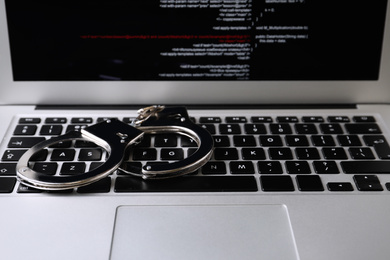 Photo of Handcuffs on modern laptop, closeup. Cyber crime