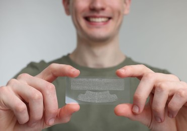Photo of Young man with whitening strips on light grey background, closeup