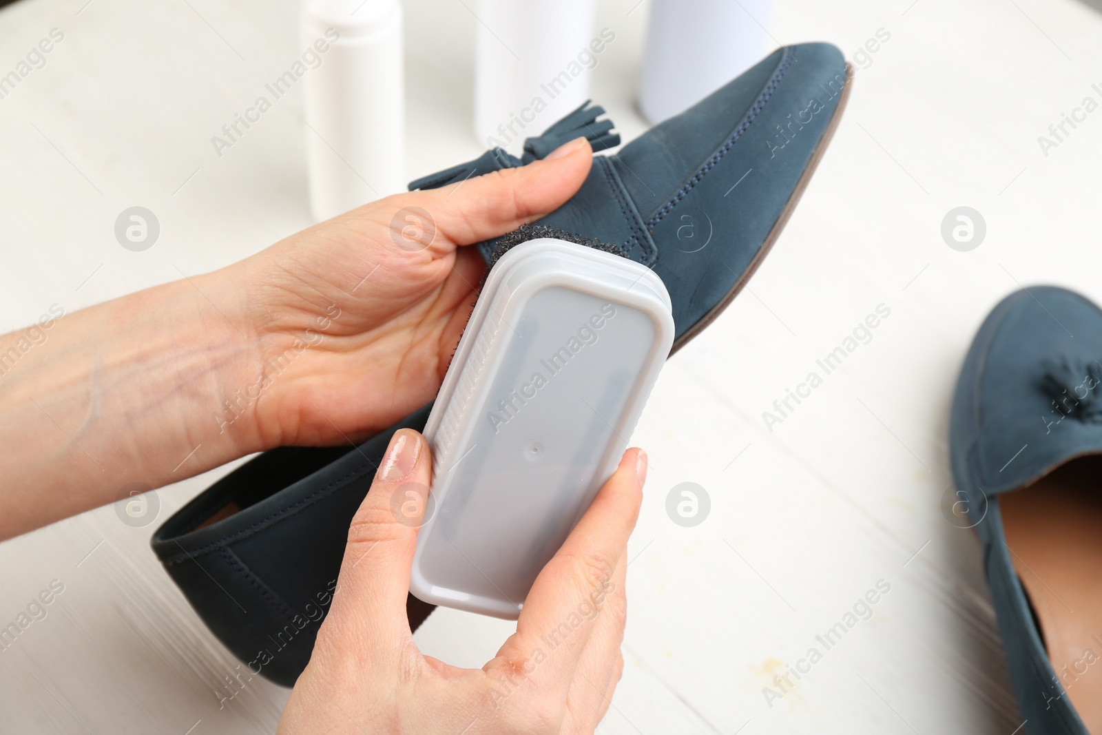 Photo of Woman taking care of stylish shoe at white table, closeup