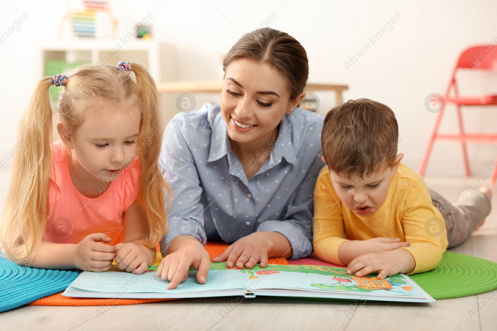 Photo of Kindergarten teacher reading book to children indoors. Learning and playing