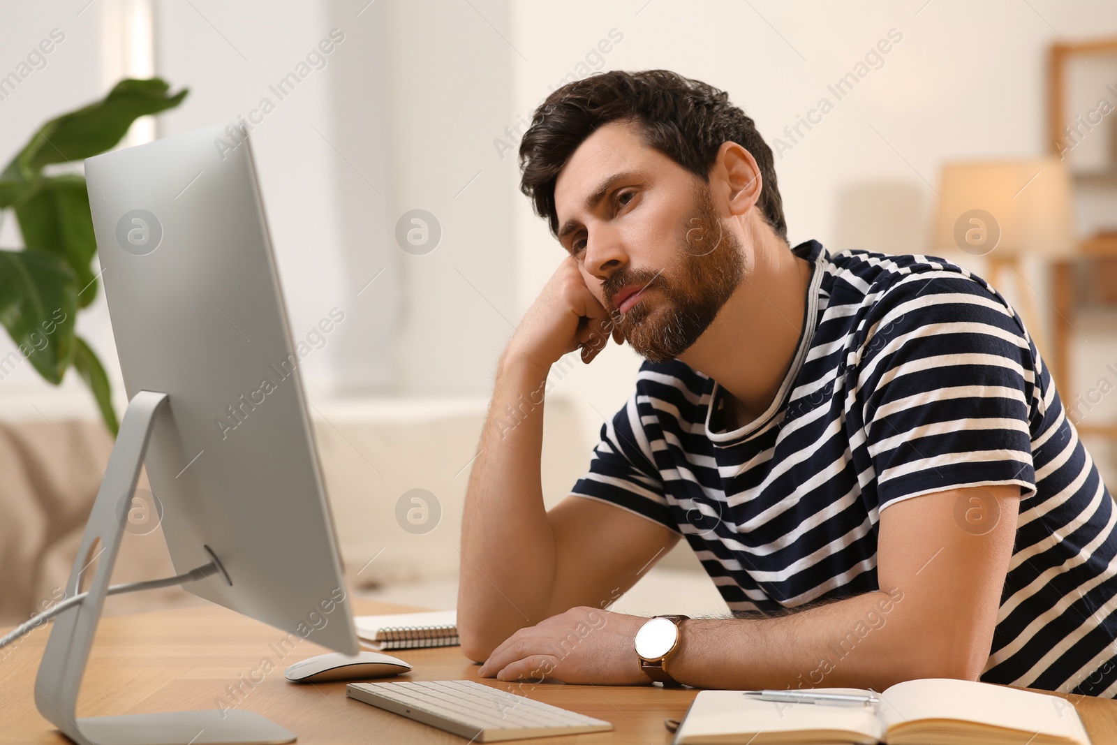 Photo of Home workplace. Tired man working with computer at wooden desk in room