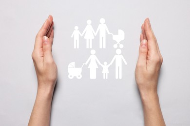 Image of Woman holding hands around cutout paper silhouette of families on light grey background, top view. Insurance concept