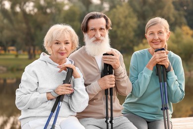 Group of senior people with Nordic walking poles sitting on wooden parapet outdoors