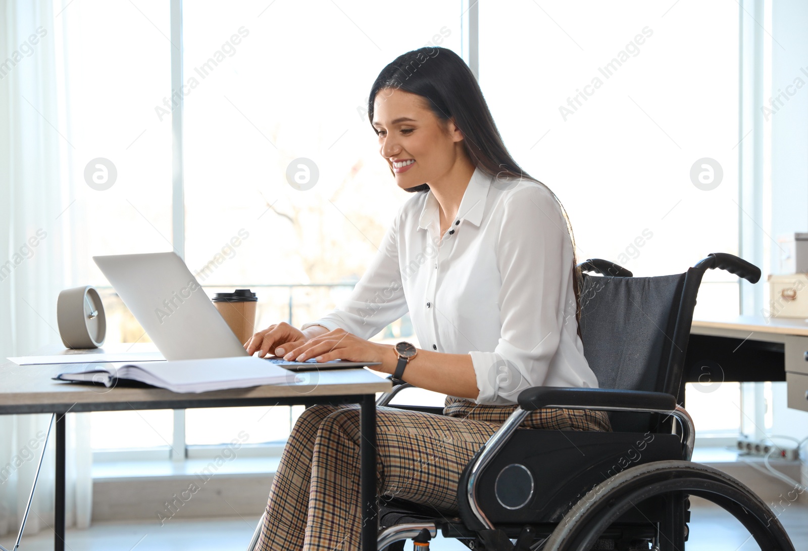 Photo of Young woman in wheelchair using laptop at workplace