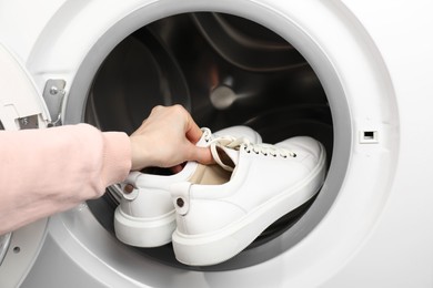 Photo of Woman putting stylish sneakers into washing machine, closeup