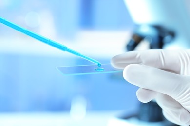 Scientist dripping sample of light blue liquid onto microscope slide in laboratory, closeup