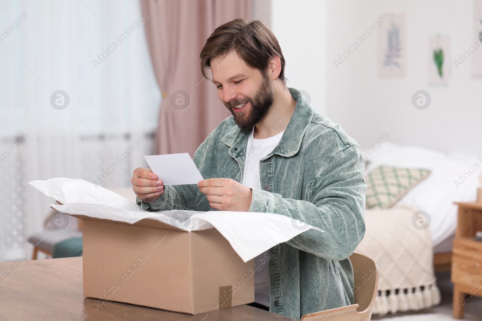 Photo of Happy man with greeting card near parcel at home. Internet shopping