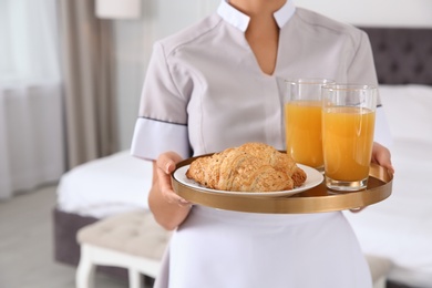 Photo of Young chambermaid holding tray with breakfast in bedroom, closeup