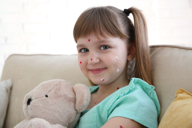 Photo of Little girl with chickenpox sitting on sofa at home