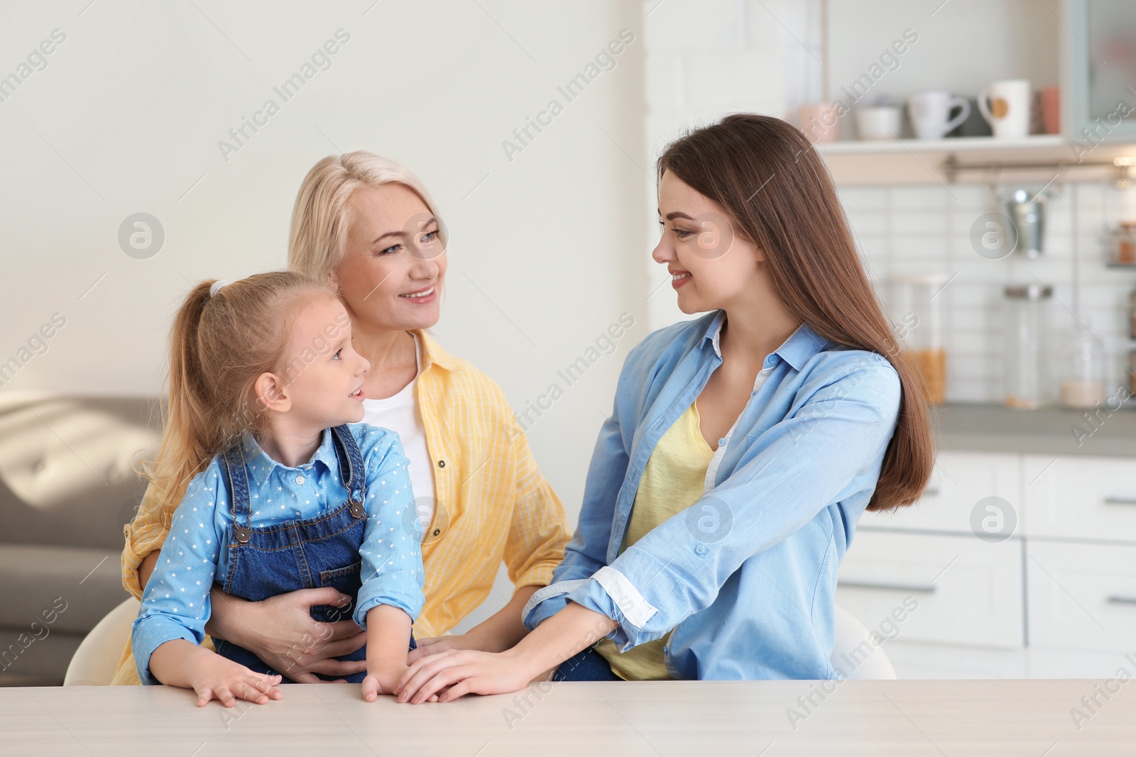 Photo of Portrait of young woman with her mother and daughter at table indoors