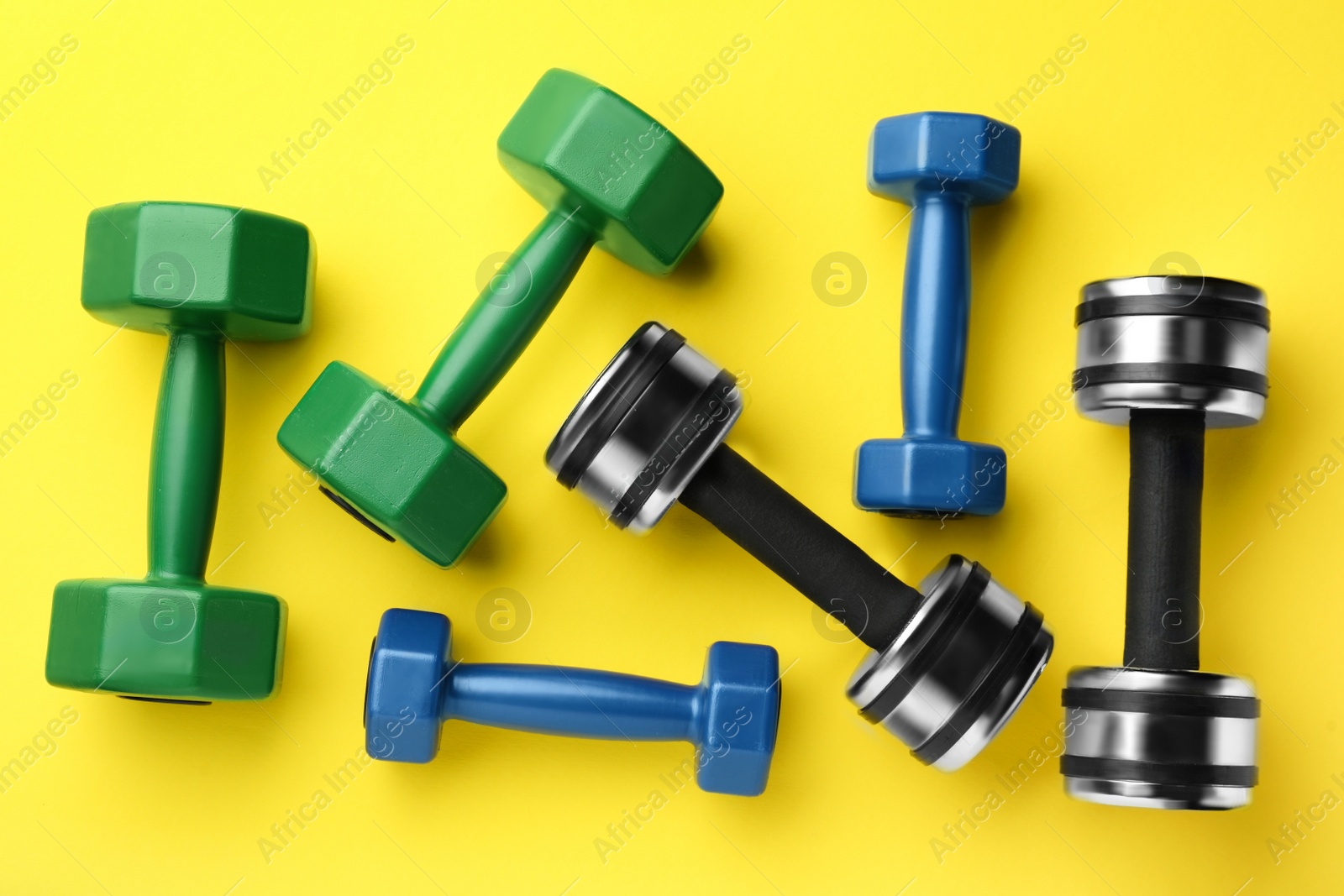 Photo of Many different stylish dumbbells on yellow background, flat lay