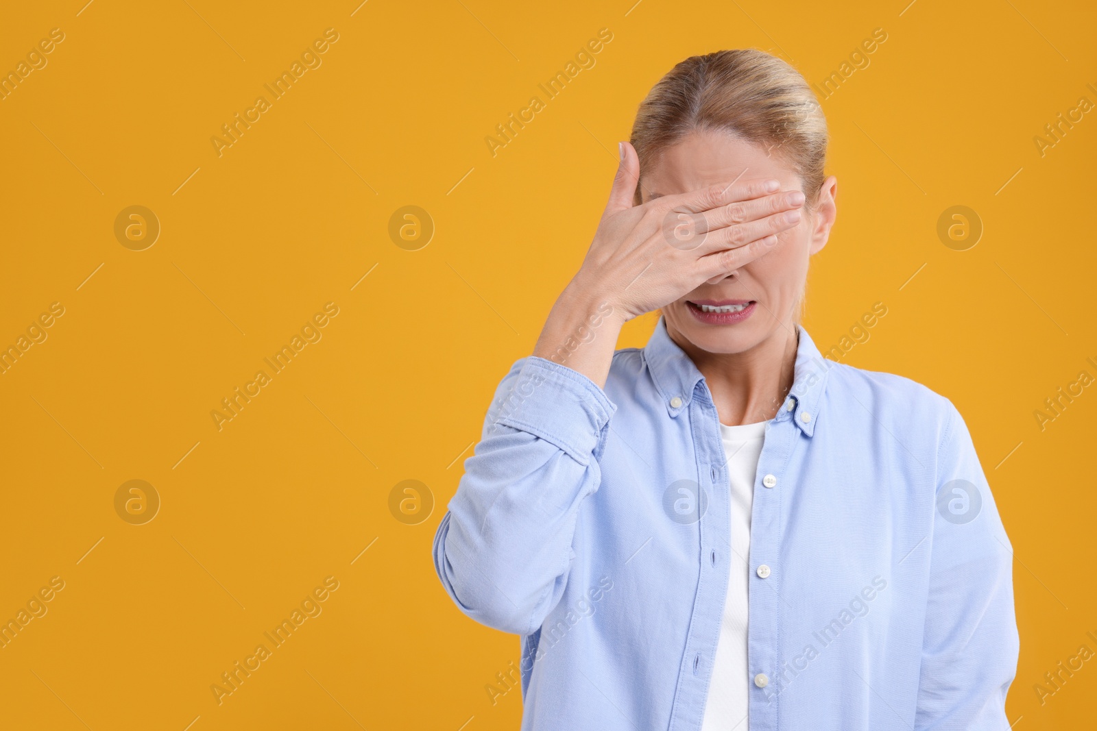 Photo of Embarrassed woman covering eyes with hands on orange background. Space for text