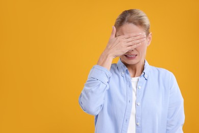 Embarrassed woman covering eyes with hands on orange background. Space for text