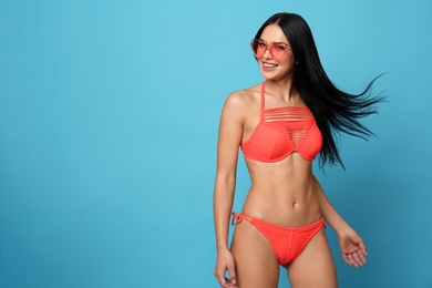 Photo of Beautiful young woman in stylish bikini with sunglasses on light blue background