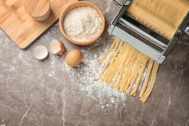 Photo of Pasta maker with dough and products on kitchen table, top view