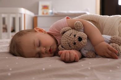 Photo of Adorable little baby with toy bear sleeping on bed at home