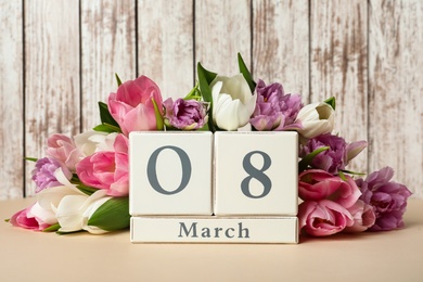 Photo of Block calendar with date 8th of March and tulips on table against wooden background. International Women's Day