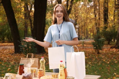 Volunteer with paper bag and food products on table in park