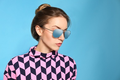Photo of Young woman wearing stylish sunglasses on blue background. Space for text