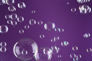 Beautiful transparent soap bubbles on purple background