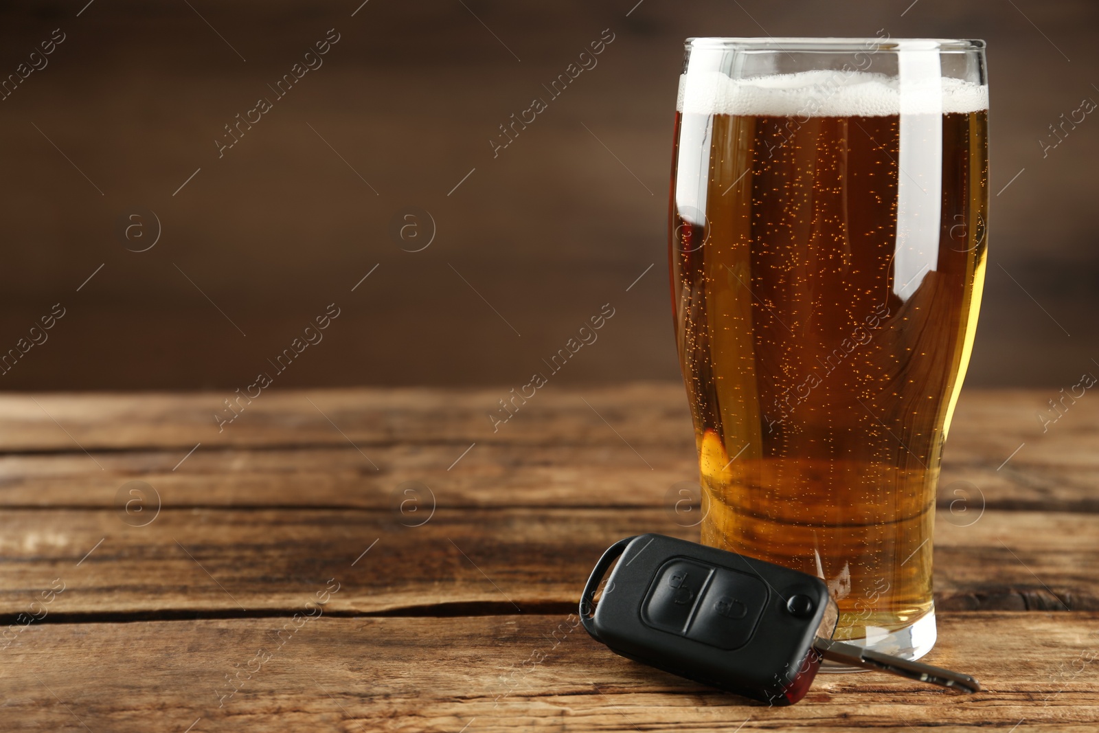 Photo of Car key near glass of alcoholic beer on wooden table, space for text. Dangerous drinking and driving