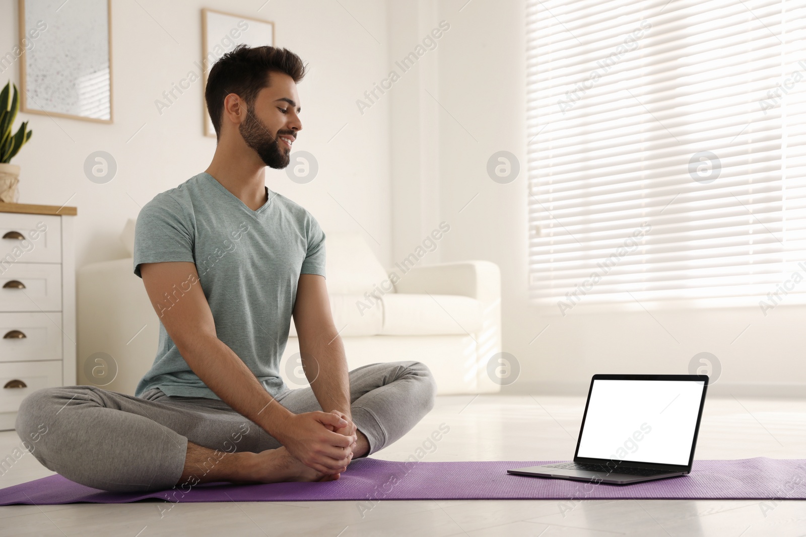 Photo of Man practicing yoga while watching online class at home during coronavirus pandemic. Social distancing