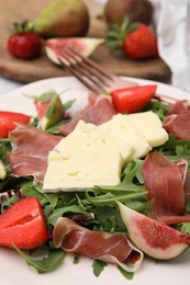 Photo of Tasty salad with brie cheese, prosciutto, strawberries and figs on white plate, closeup