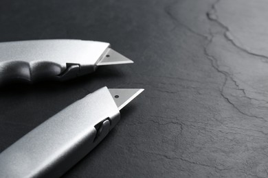 Photo of Two utility knives on black table. Space for text