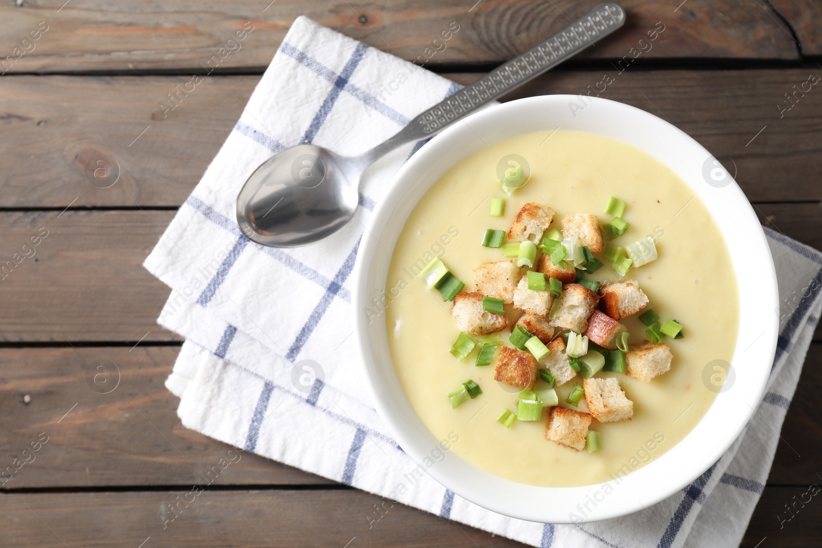 Photo of Tasty potato soup with croutons in bowl and spoon on wooden table, flat lay