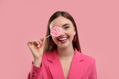 Photo of Beautiful woman in pink clothes covering eye with lollipop on color background