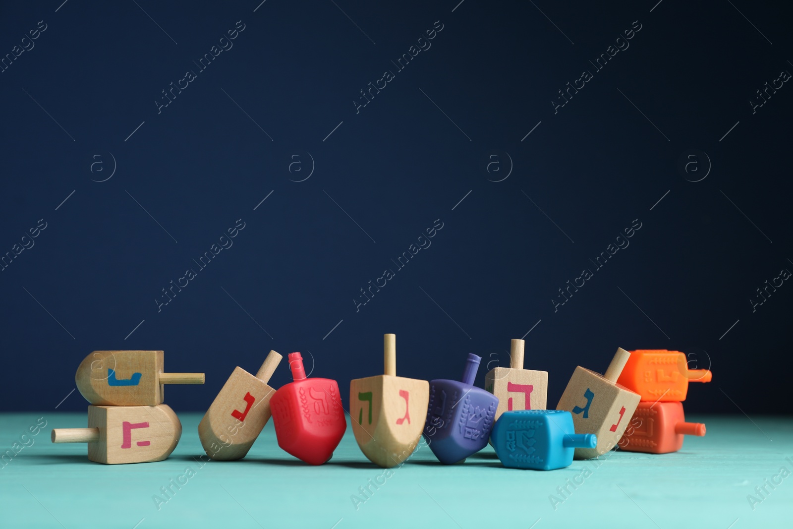 Photo of Different dreidels on light blue table against purple background, space for text. Traditional Hanukkah game