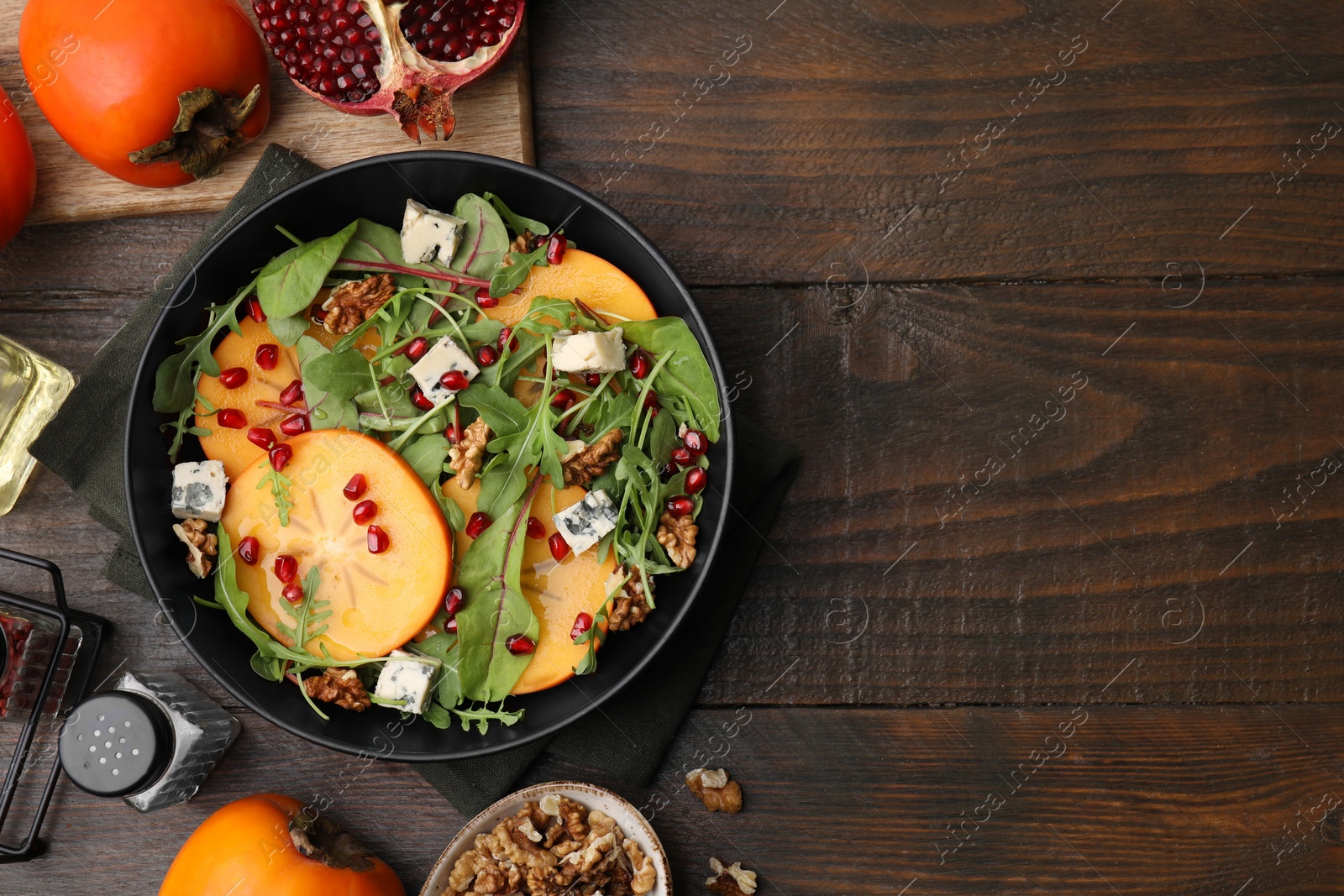 Photo of Tasty salad with persimmon, blue cheese, pomegranate and walnuts served on wooden table, flat lay. Space for text