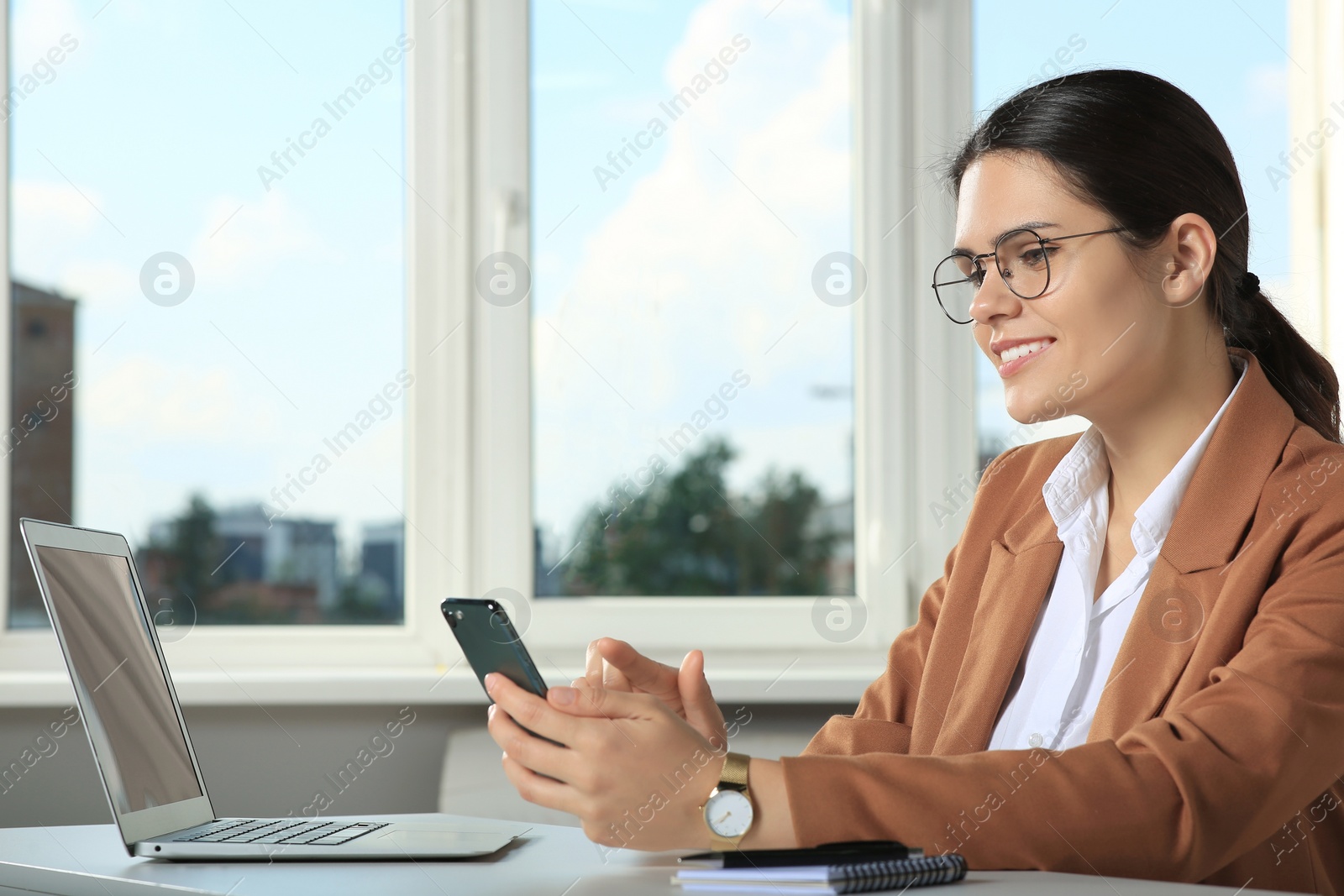 Photo of Young woman using smartphone at table in office