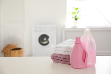 Stack of clean towels and detergents on white table indoors. Space for text