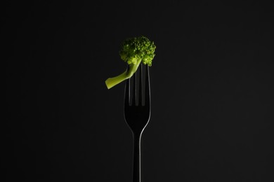 Photo of Fork with tasty broccoli on black background
