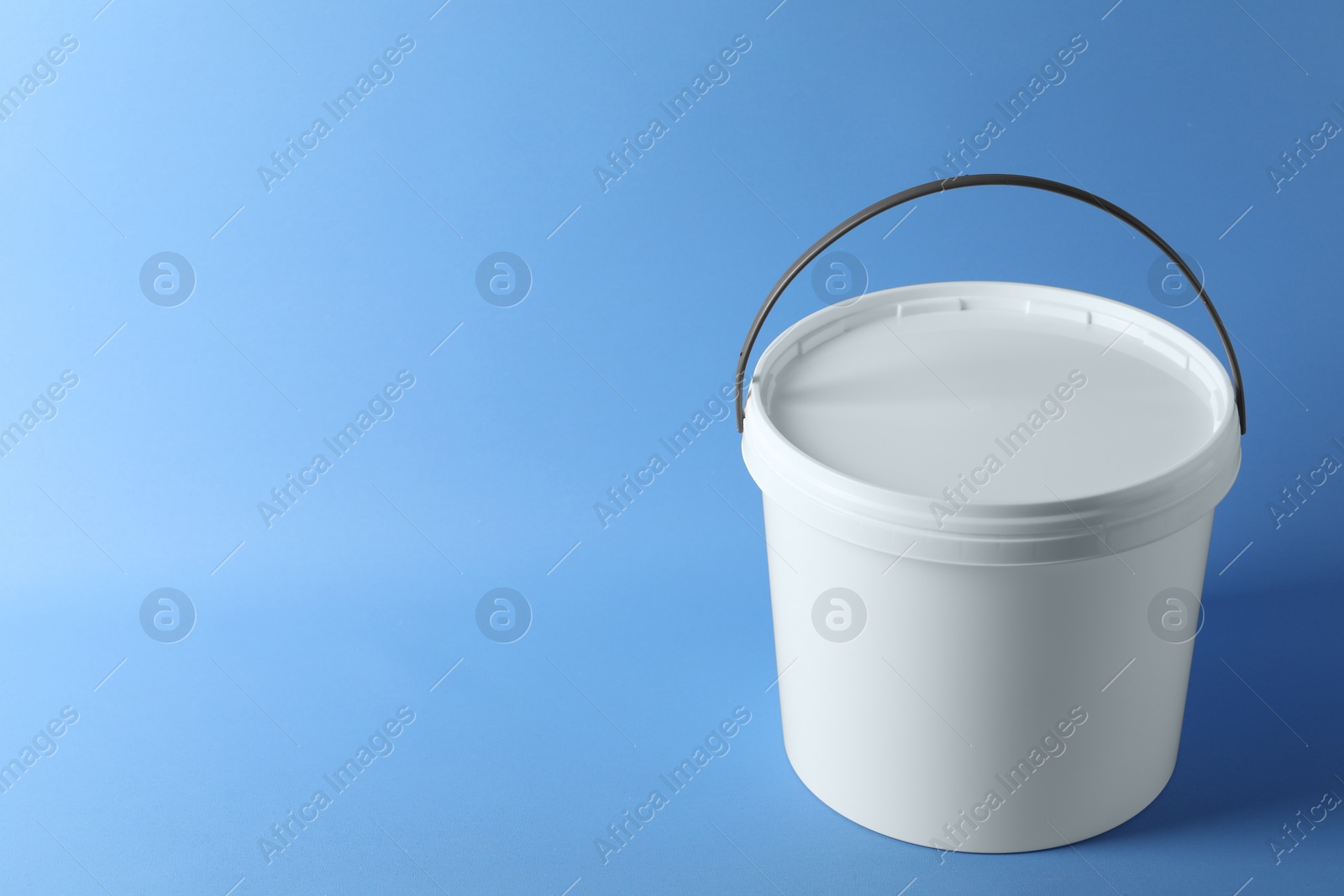 Photo of One plastic bucket with lid on light blue background. Space for text