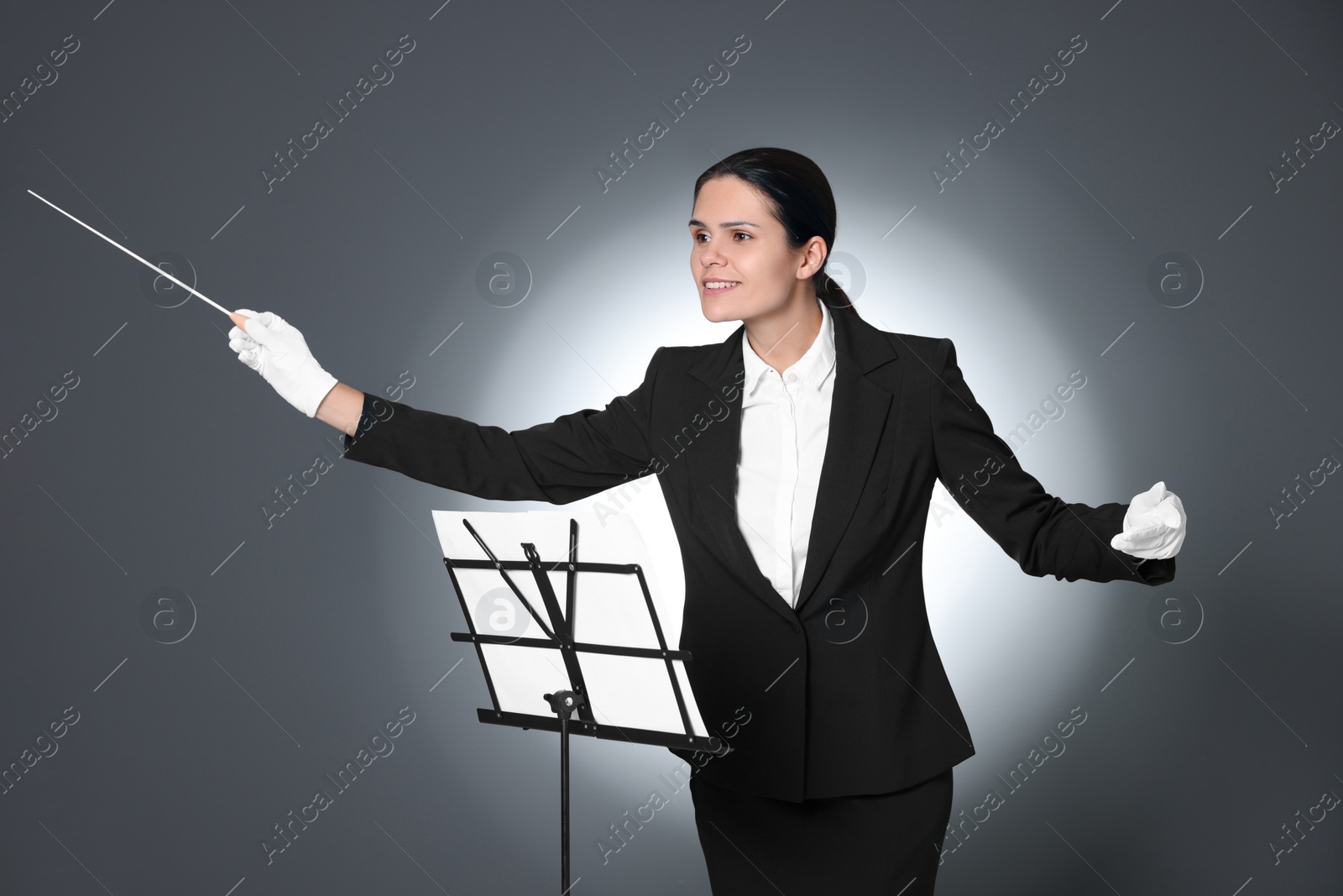 Photo of Happy professional conductor with baton and note stand on grey background