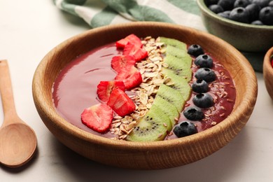 Photo of Bowl of delicious smoothie with fresh blueberries, strawberries, kiwi slices and oatmeal on white marble table