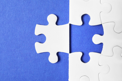 Photo of Blank white puzzle with separated piece on blue background, flat lay
