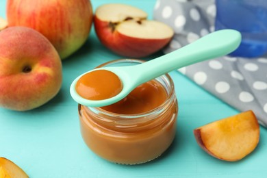 Photo of Spoon with healthy baby food and glass jar on turquoise wooden table, closeup