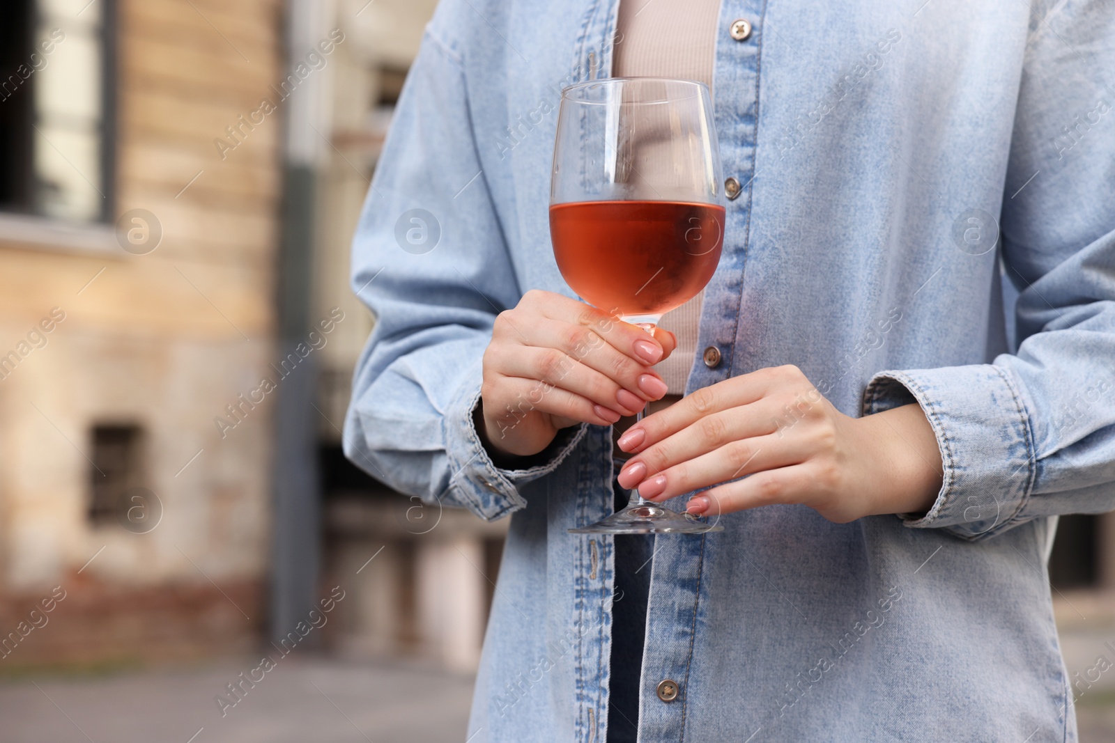 Photo of Woman holding glass of rose wine outdoors, closeup. Space for text