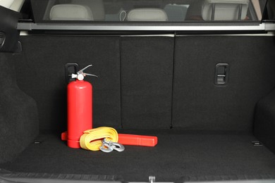 Photo of Red fire extinguisher, towing strap and foldable emergency warning triangle in trunk, space for text. Car safety