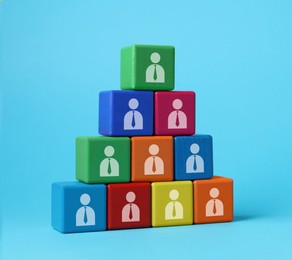 Team and management concept. Pyramid of colorful cubes with human icons on light blue background