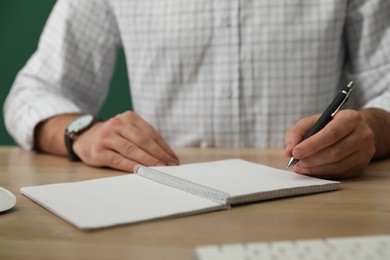Photo of Left-handed man writing in notebook at wooden table, closeup