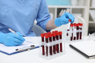 Photo of Laboratory testing. Doctor with blood samples in tubes at white table indoors, closeup