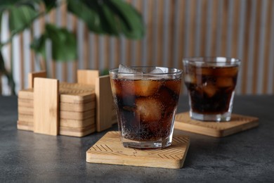 Glasses of cold drink with stylish cup coasters on grey table