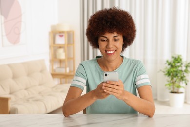 Happy young woman with smartphone sitting at table indoors