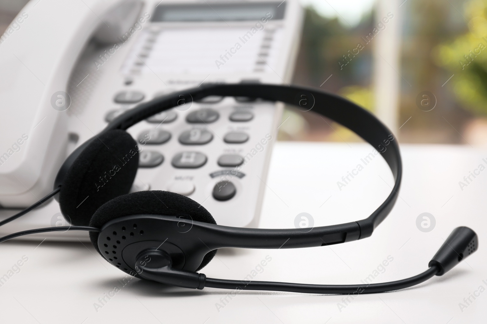 Photo of Headset and desk phone on table indoors. Technical support concept