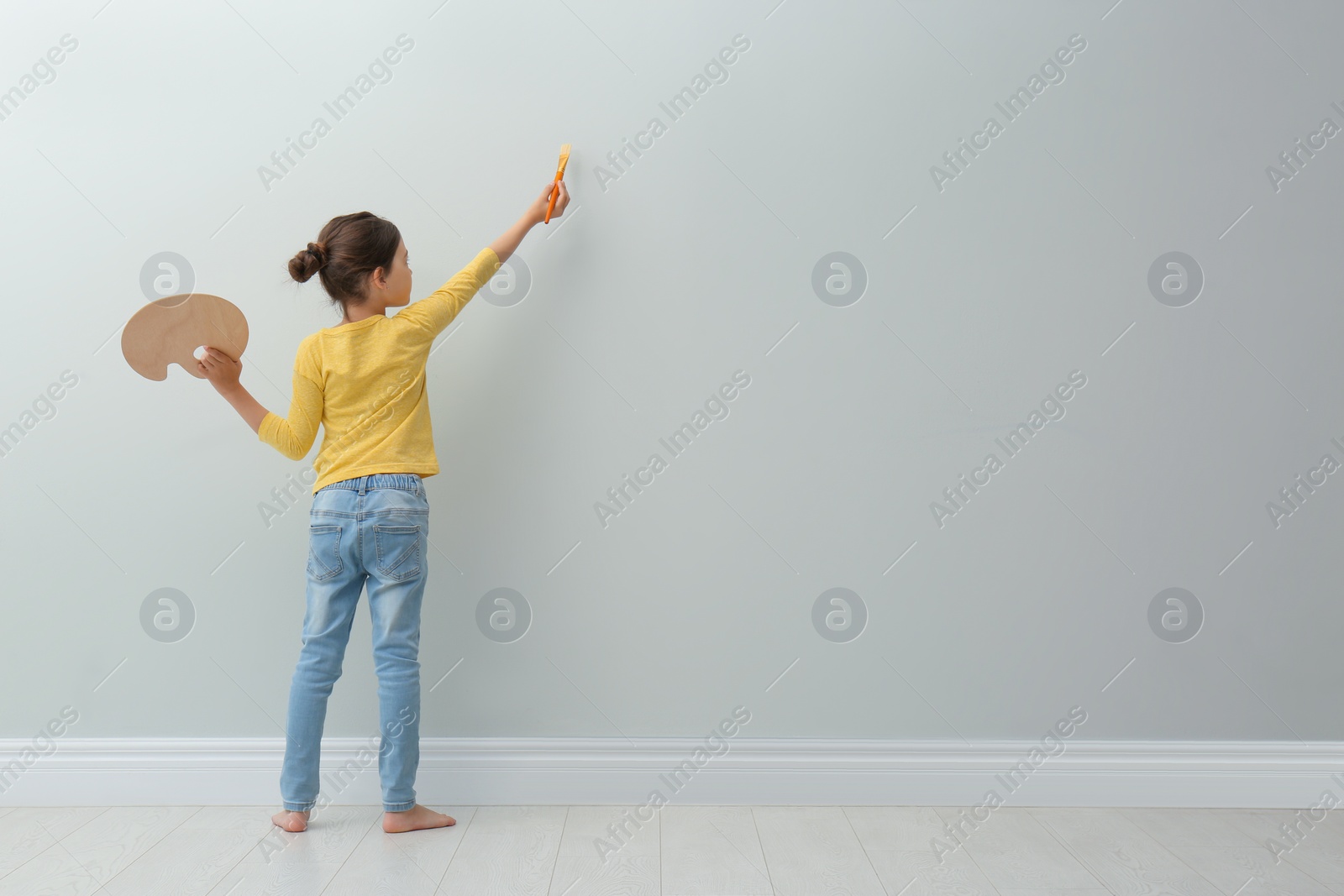 Photo of Little girl painting on light grey wall indoors, back view. Space for text