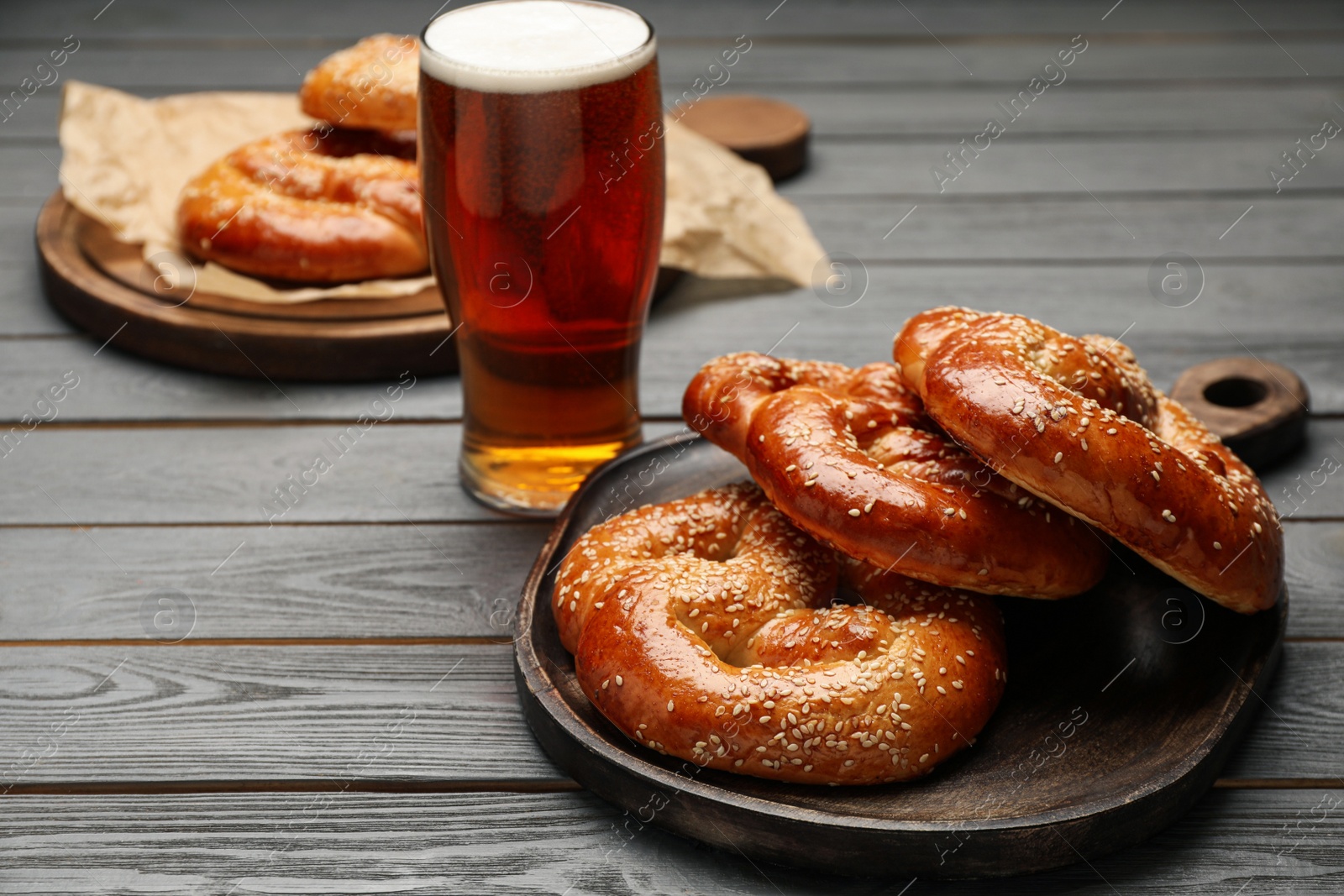 Photo of Tasty freshly baked pretzels and glass of beer on grey wooden table. Space for text